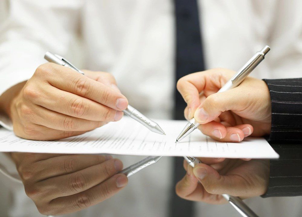 Two people are signing papers on a table.